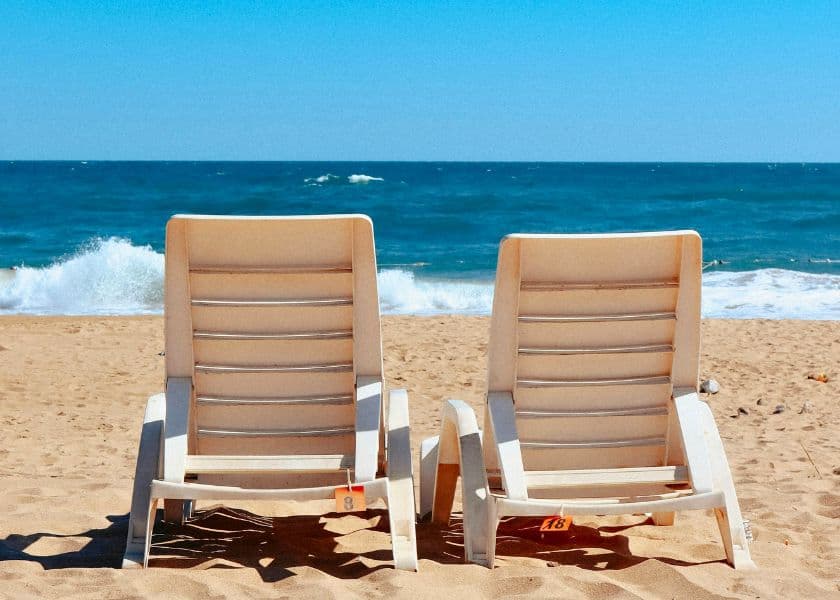 Two white lounge chairs facing the ocean on a sandy beach. Two white lounge chairs facing the ocean on a sandy beach.