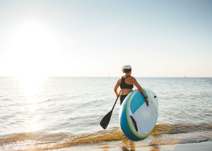 A person carries a paddleboard toward the water during sunset. A person carries a paddleboard toward the water during sunset.