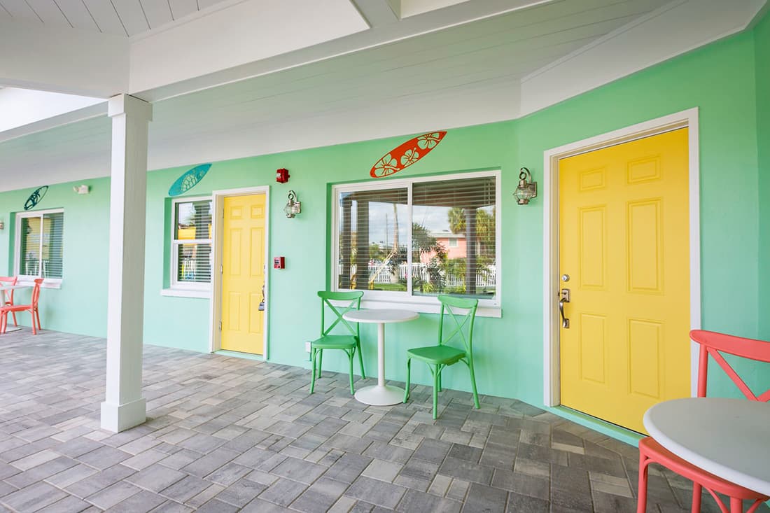 A vibrant courtyard features yellow doors, green and orange decor, and a small table with colorful chairs.
