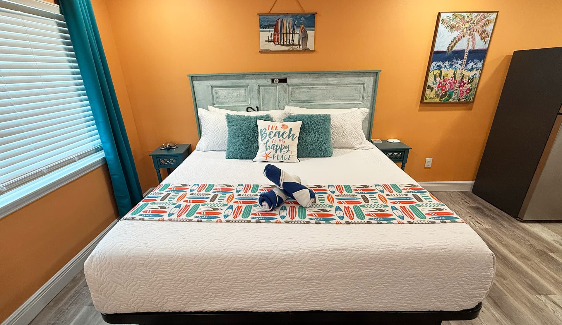 A neatly arranged bed with colorful pillows and a beach-themed decorative strip against an orange wall.
