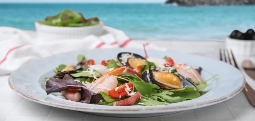A colorful seafood salad is presented on a plate with a beach backdrop.
