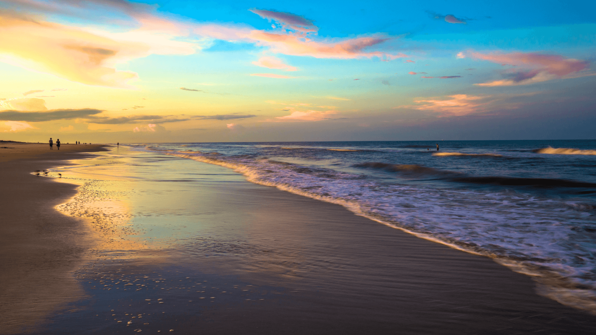 A tranquil beach scene at sunset with gentle waves and colorful clouds.