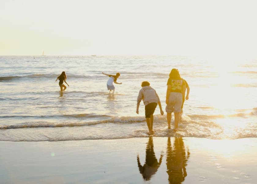 Four people play in the waves at sunset on a beach.