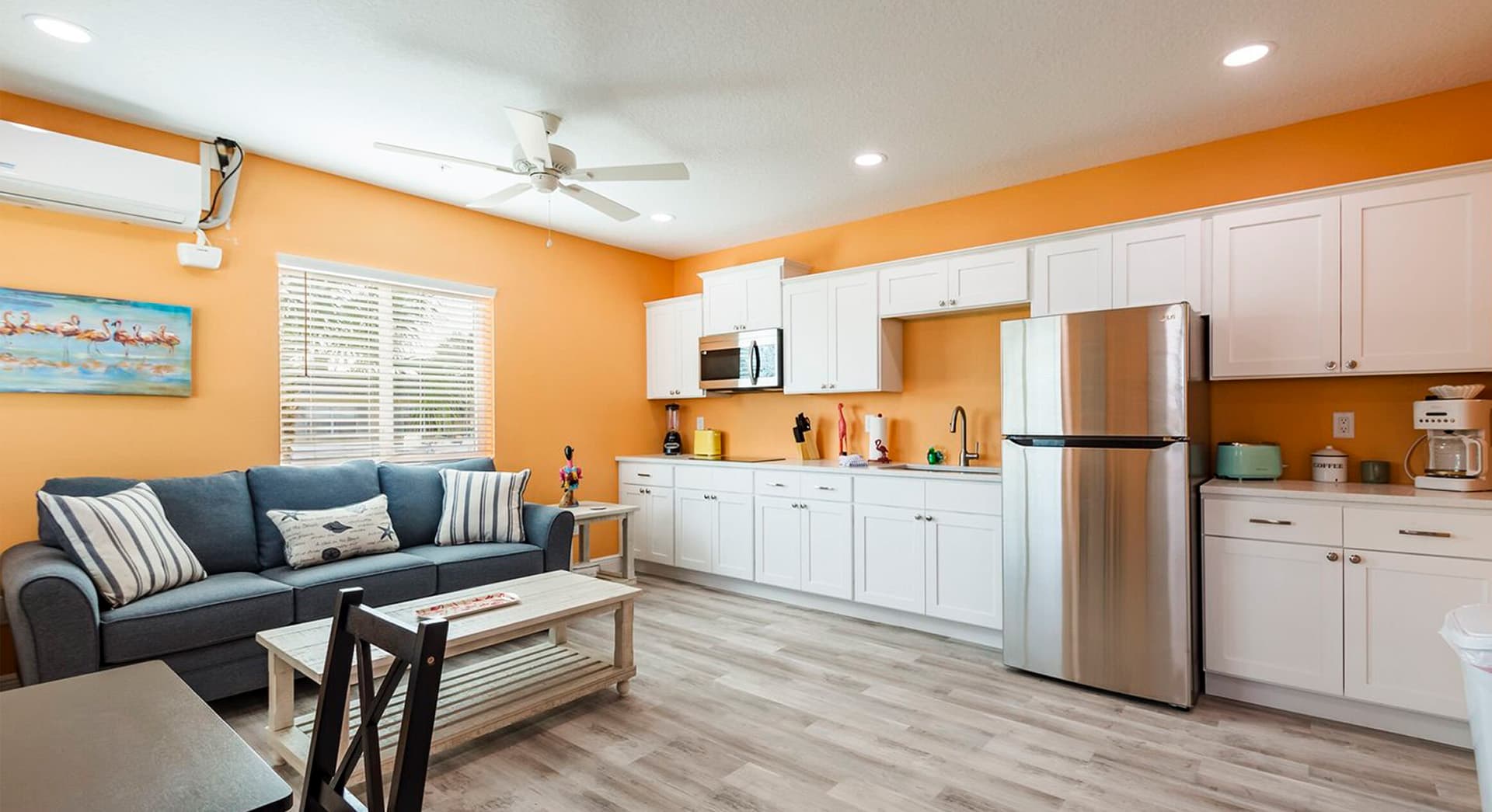 Bright orange living space with a cozy sofa, kitchen area, and wooden dining table.