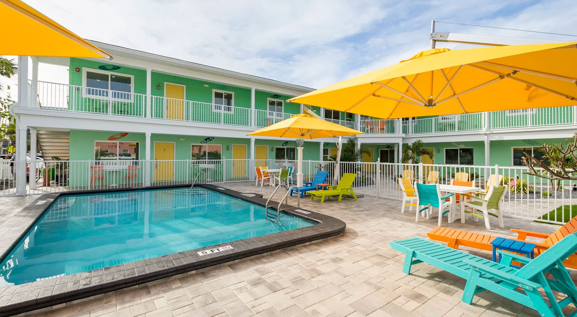 A vibrant pool area surrounded by colorful chairs and umbrellas at a motel with green and yellow accents.